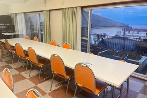 A conference room with a long table and chairs, large windows with curtains, and a view of the outside. - Yu-no-izumi (Ito)