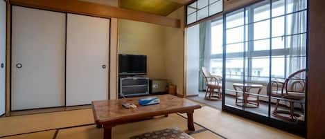 Una habitación japonesa tradicional con suelo de tatami, una mesa baja, un cojín, un televisor y puertas correderas.