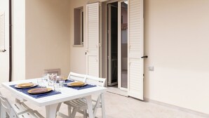 A dining table set with plates, glasses, and cutlery, with white chairs and a tiled floor. - Casa Marina con Patio by Wonderful Italy (Olbia)
