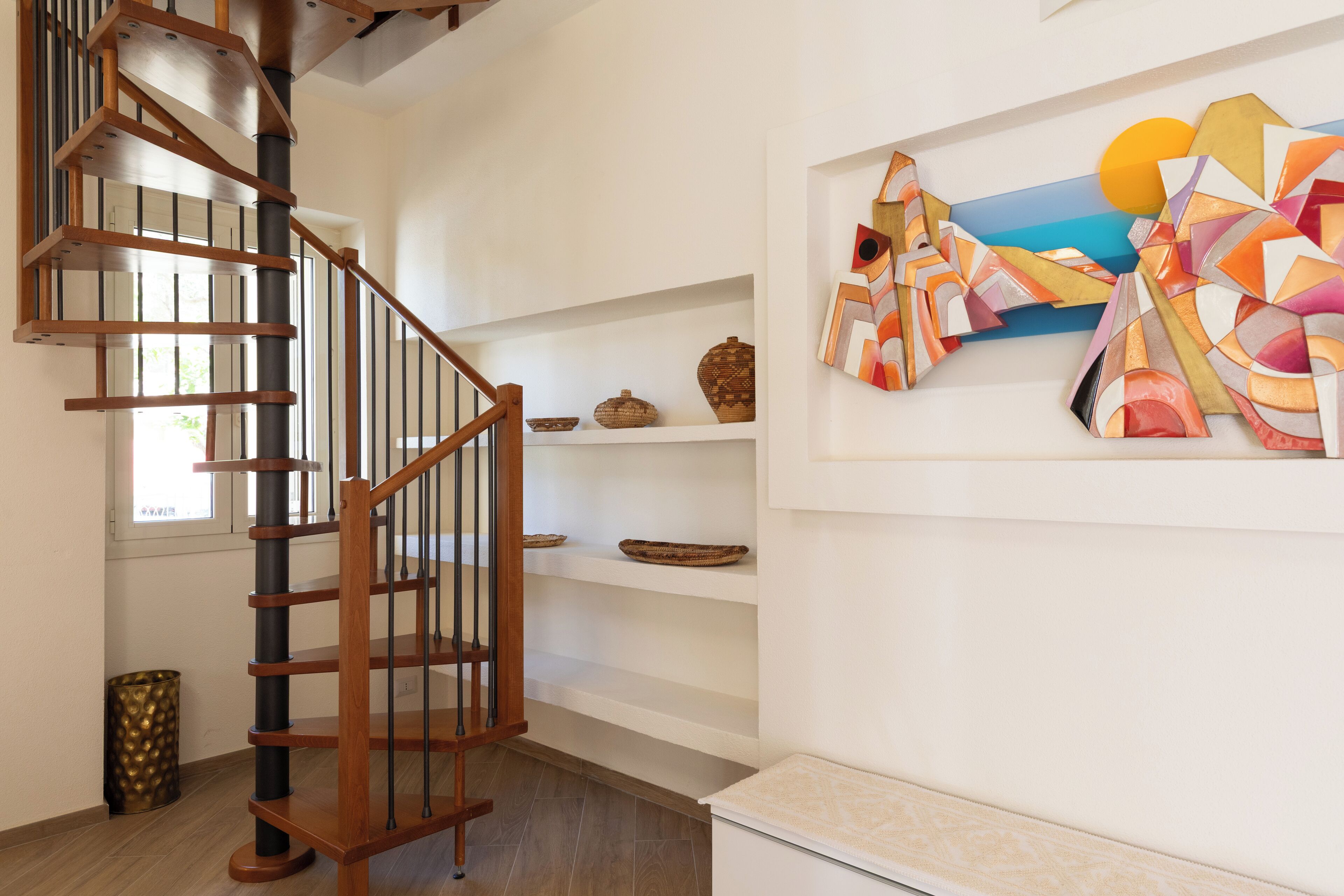 A spiral staircase with wooden railings and a modern art piece on the wall.
