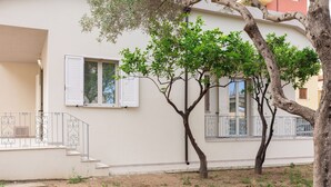 A building with a white exterior, a balcony with metal railings, and a tree in front. - Casa Marina con Patio by Wonderful Italy (Olbia)