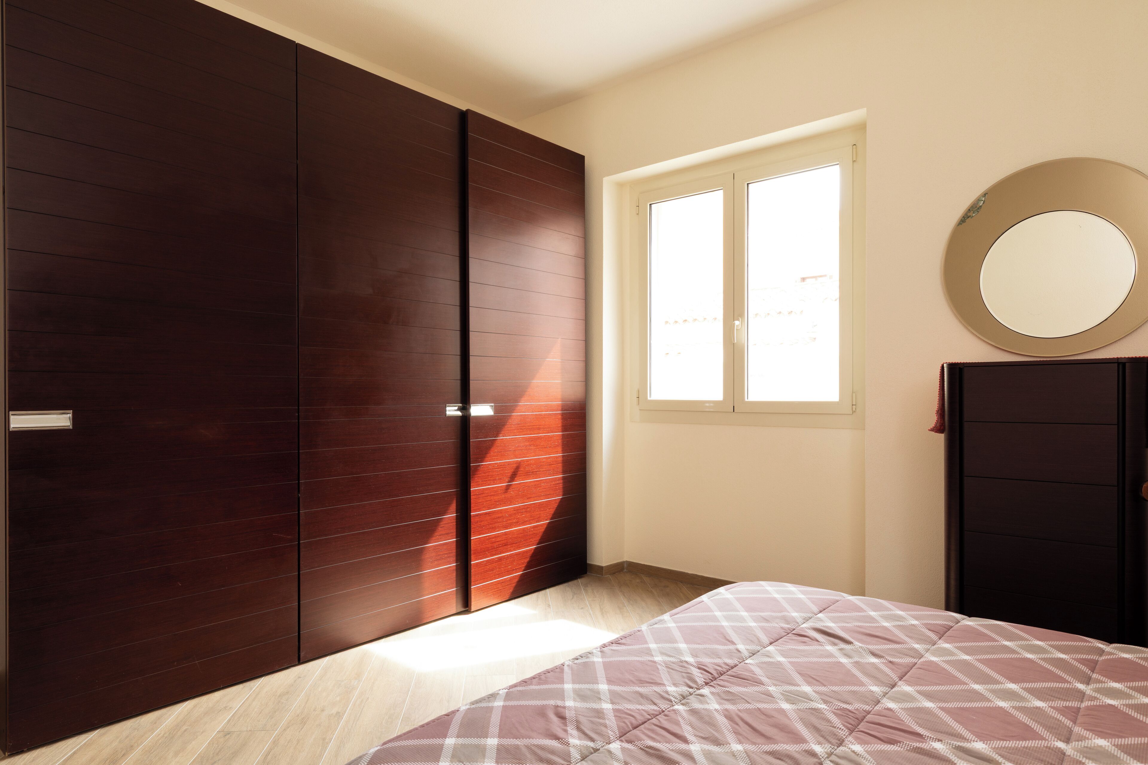 Une chambre à coucher avec un lit, une armoire, un miroir et une fenêtre.