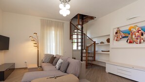 A modern living room with a sofa, a staircase, a flat-screen TV, and a floor lamp. - Casa Marina con Patio by Wonderful Italy (Olbia)