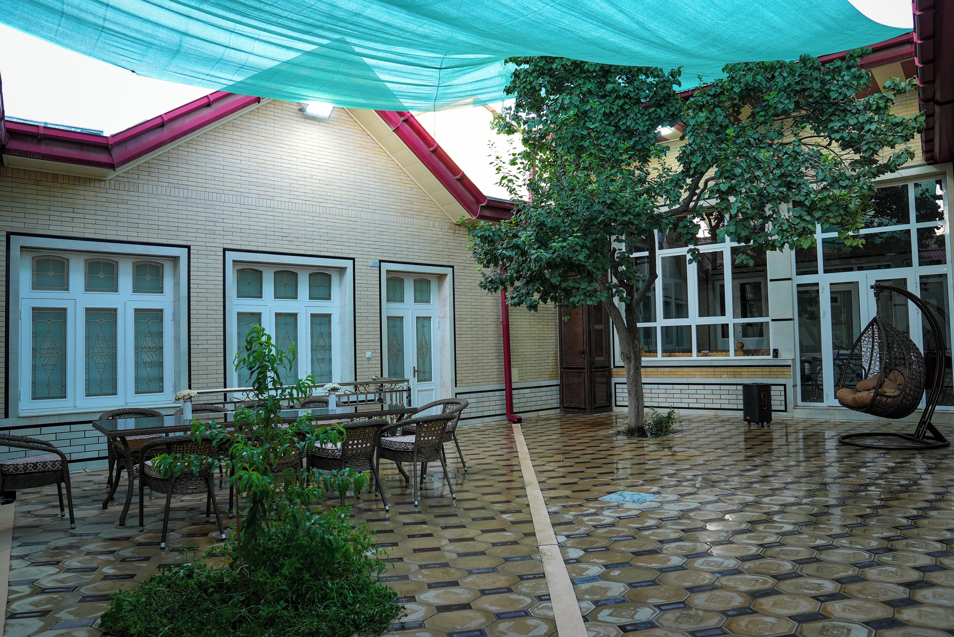 A covered patio area with tiled flooring, outdoor furniture, and a hanging chair.