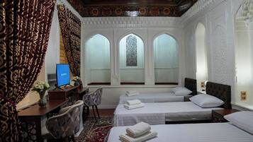 A hotel room with three beds, a desk with a computer, a chair, and a large window with intricate patterns.