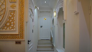 Un pasillo estrecho con una puerta blanca al final, una barandilla y paneles decorativos en las paredes.