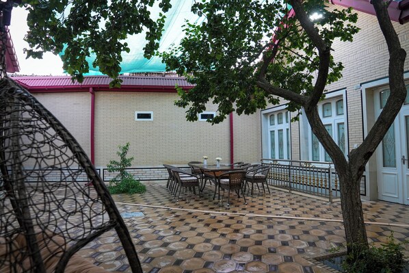 A courtyard with a tiled floor, a round table with chairs, and a tree. - Learmara Guest House (Samarkand)
