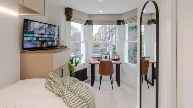 A modern bedroom with a bed, a desk, and a large mirror. - Kensington Standard Room (London)