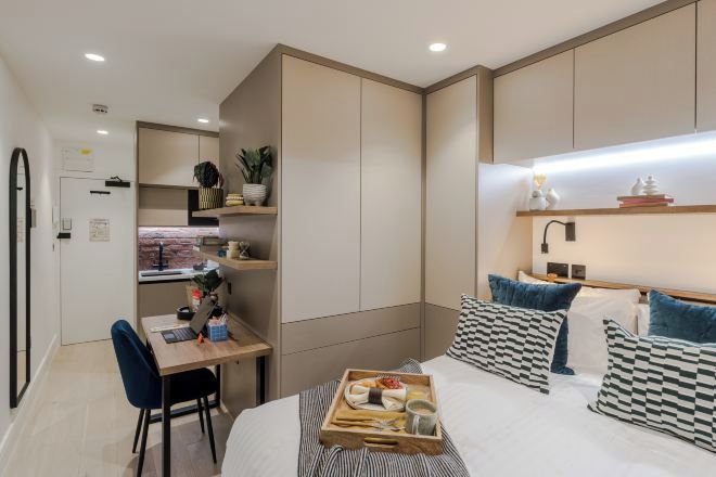 A modern hotel room with a bed, bedside table, and a desk with a chair.