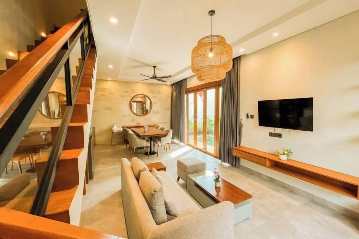 A modern living room with a staircase, a dining area, a sofa, a coffee table, a TV, and a large window.