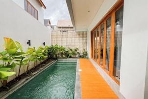 A modern house with a small swimming pool, a wooden deck, and a glass door leading to a covered area.