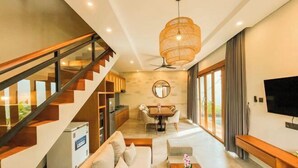 A modern living room with a staircase, a dining area, and a TV. - KANGIN House Sanur (Bali)