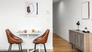 Un comedor moderno con dos sillones de cuero, una mesa blanca y una decoración minimalista que incluye un cuadro enmarcado y un aparador con una lámpara.
