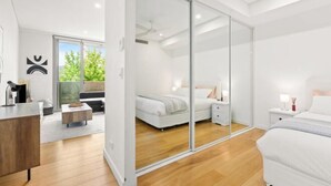 Un dormitorio moderno con una puerta corrediza de vidrio que da a un balcón, una cama grande, una mesita de noche y una zona de escritorio con una silla.