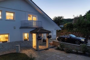 Une maison à deux étages avec un balcon, une terrasse couverte et une voiture garée.