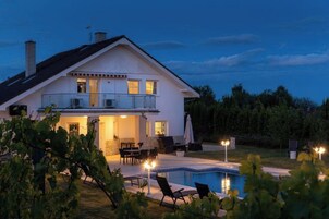 Una casa de dos pisos con piscina, mobiliario exterior y un patio bien iluminado.
