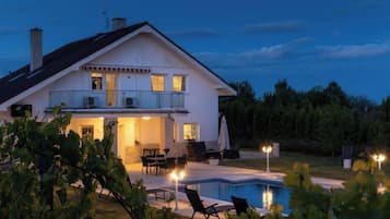 Ein zweistöckiges Haus mit Swimmingpool, Sitzgelegenheit im Freien und einer gut beleuchteten Terrasse.