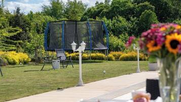 A garden with a swing set, outdoor seating, and a pathway leading to a table with a vase of flowers.