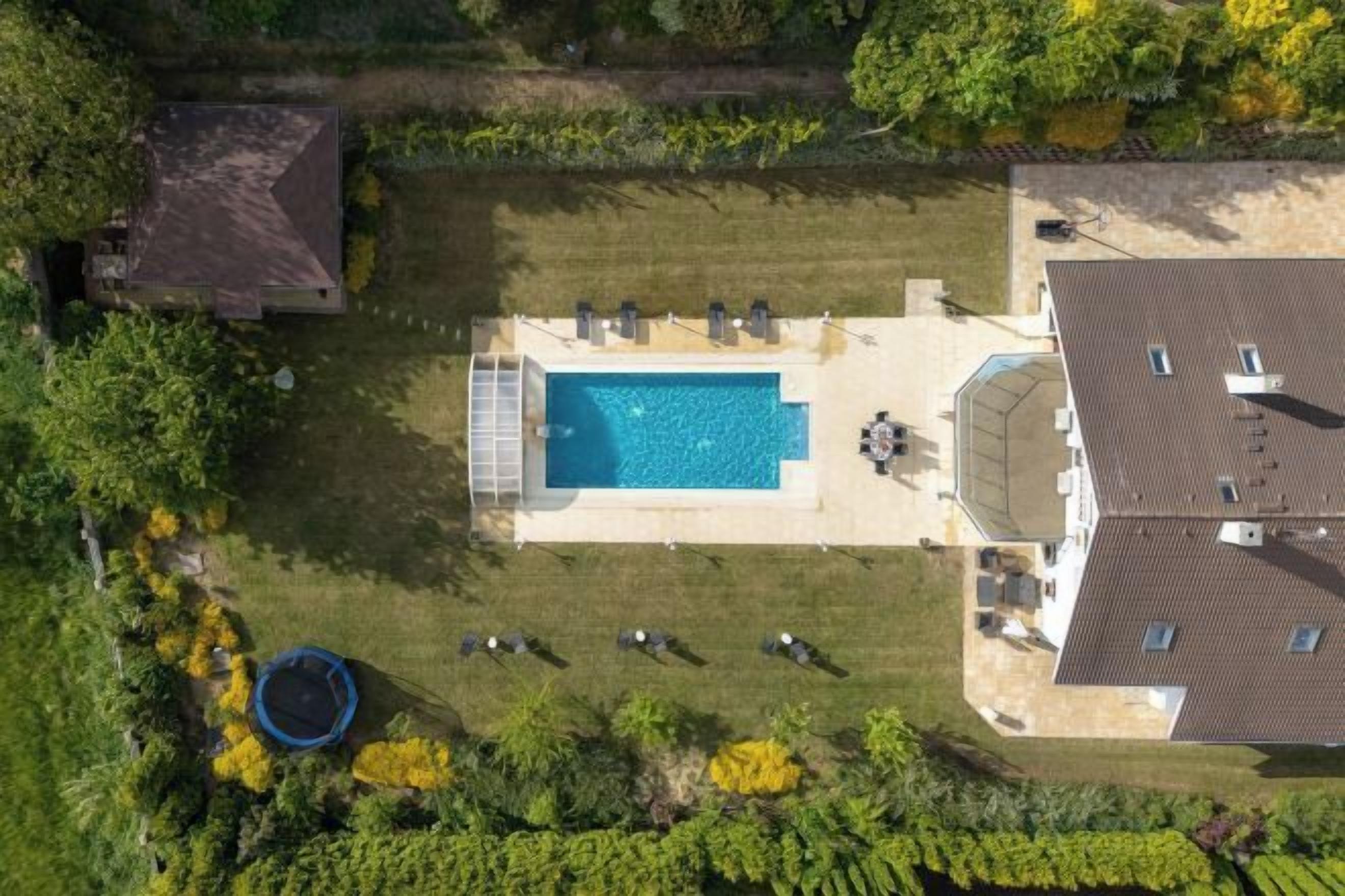 An aerial view of a property with a swimming pool, a covered patio area, and a fenced yard.