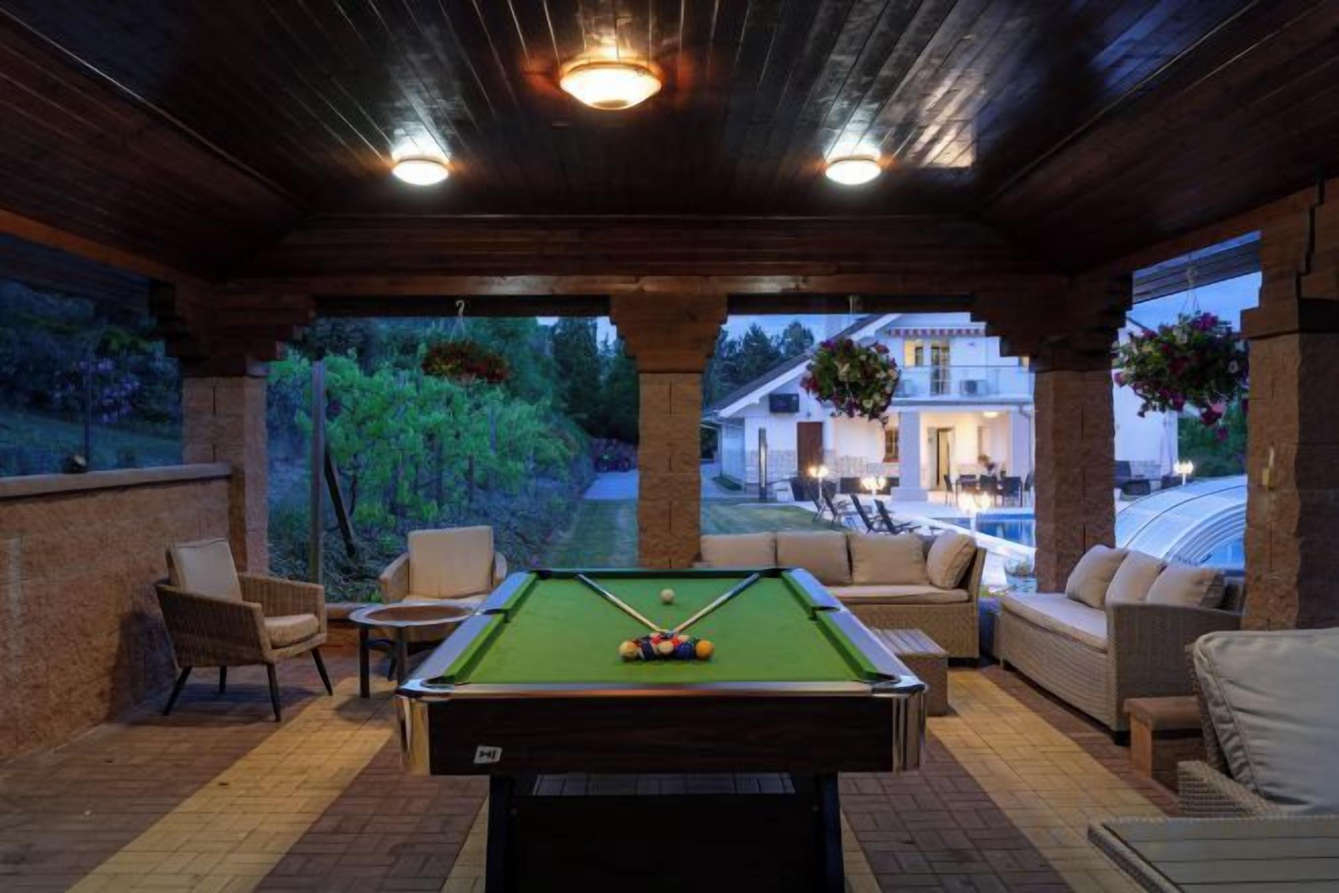 Un espace piscine intérieur comprenant une table de billard, des sièges et une vue sur une maison.