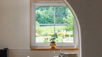 A dining area with a table set for two, a vase with flowers, and a window with a view of a garden.