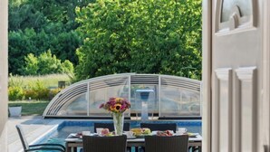 Un espace aménagé au bord de la piscine, avec une table pour deux, une véranda et une vue sur une végétation luxuriante.