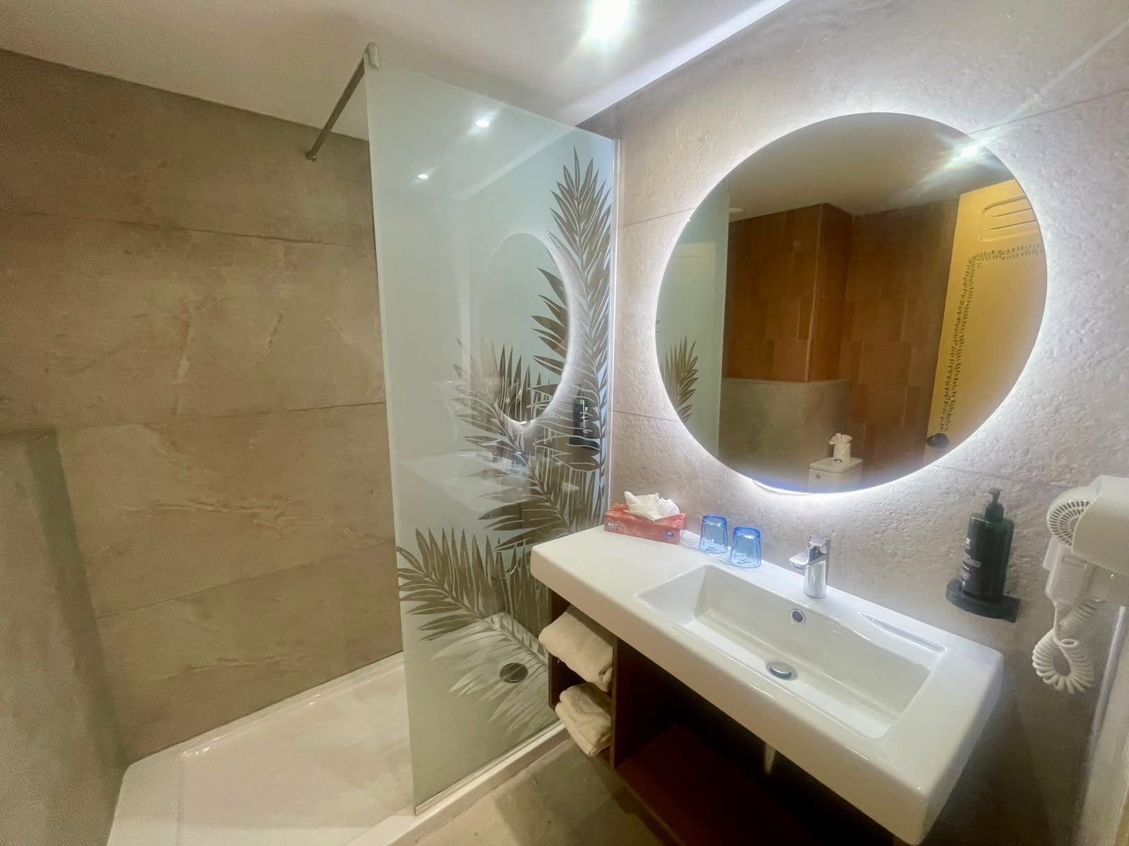 Un bagno moderno con box doccia in vetro, lavandino bianco e specchio rotondo.