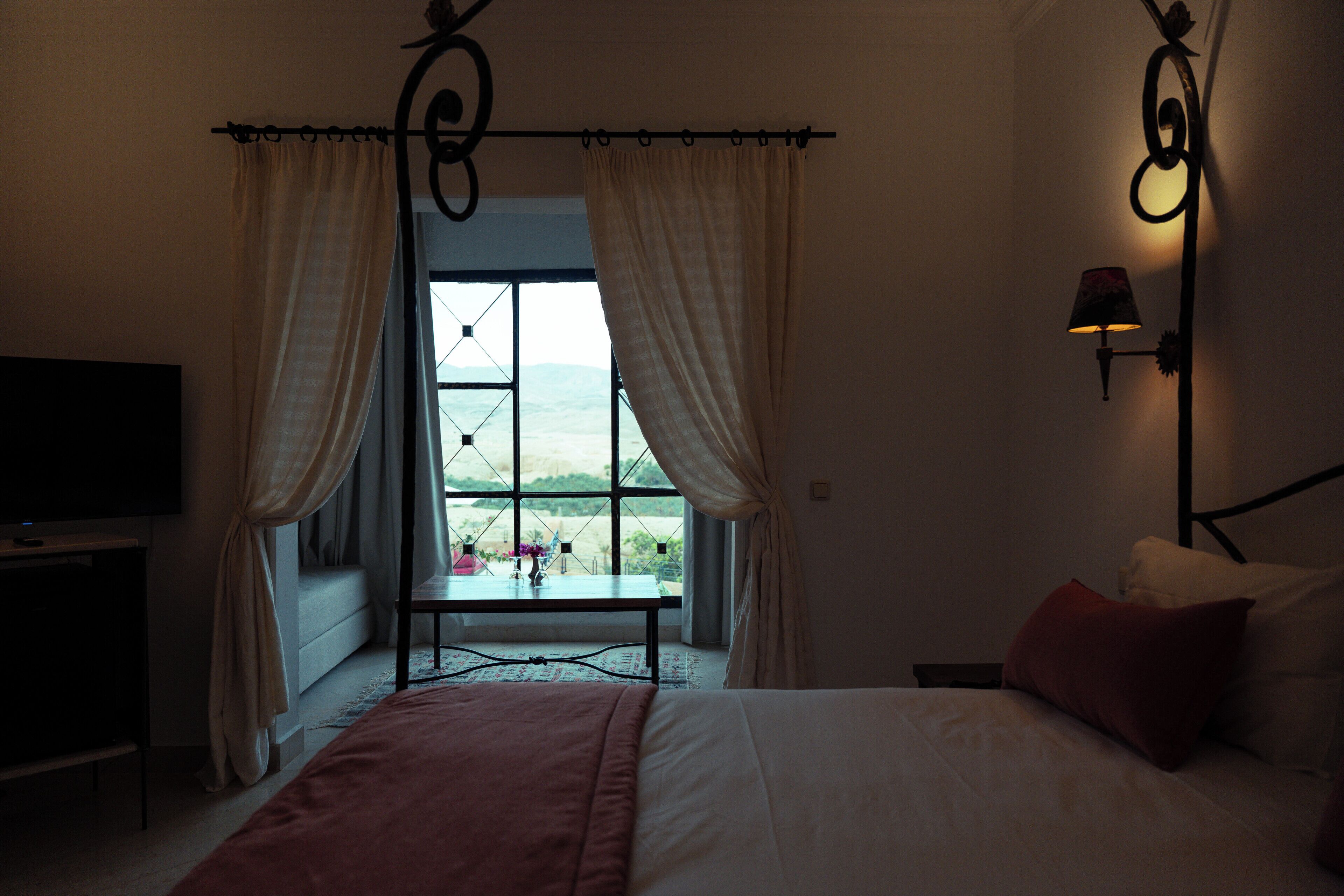 A bedroom with a bed, a TV, a window with curtains, and a lamp.