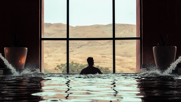 Una persona en una bañera con vistas a un paisaje desértico a través de amplias ventanas.