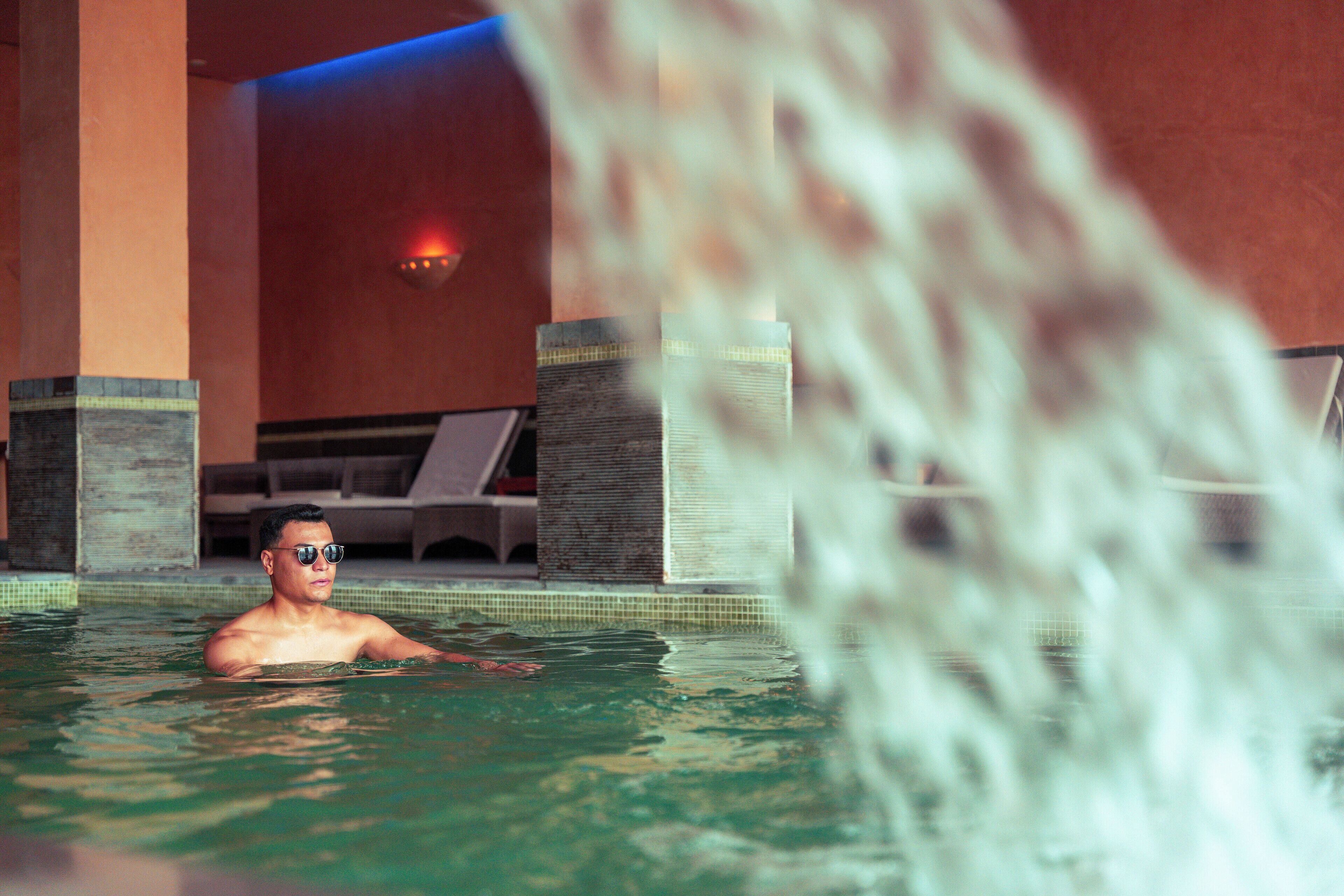 Un homme dans une piscine, avec une cascade en arrière-plan.