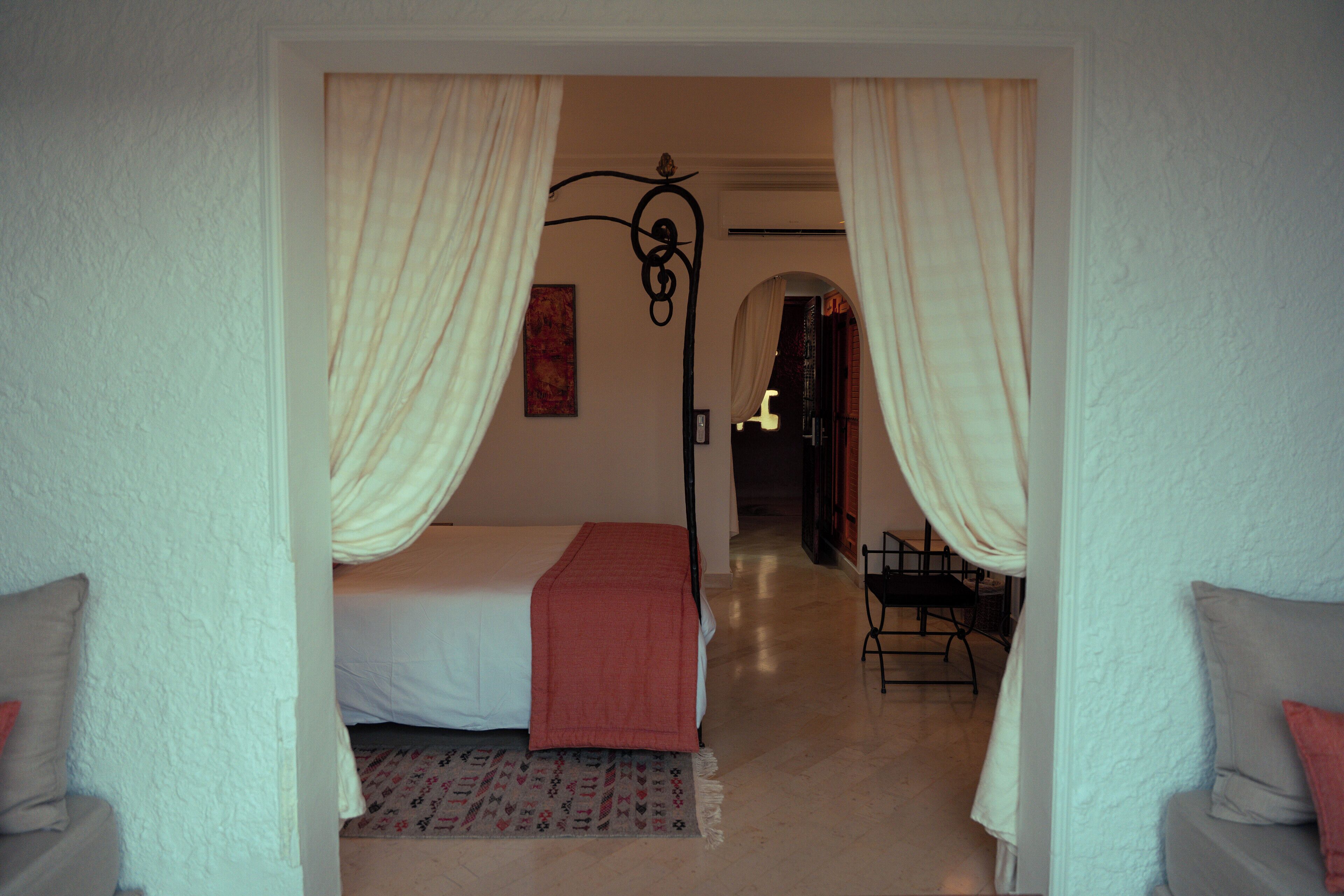 A bedroom with a bed, a nightstand, a chair, and a window with curtains.