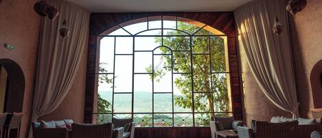 A spacious room with a large arched window offering a scenic view, wicker furniture, and a modern ceiling design.