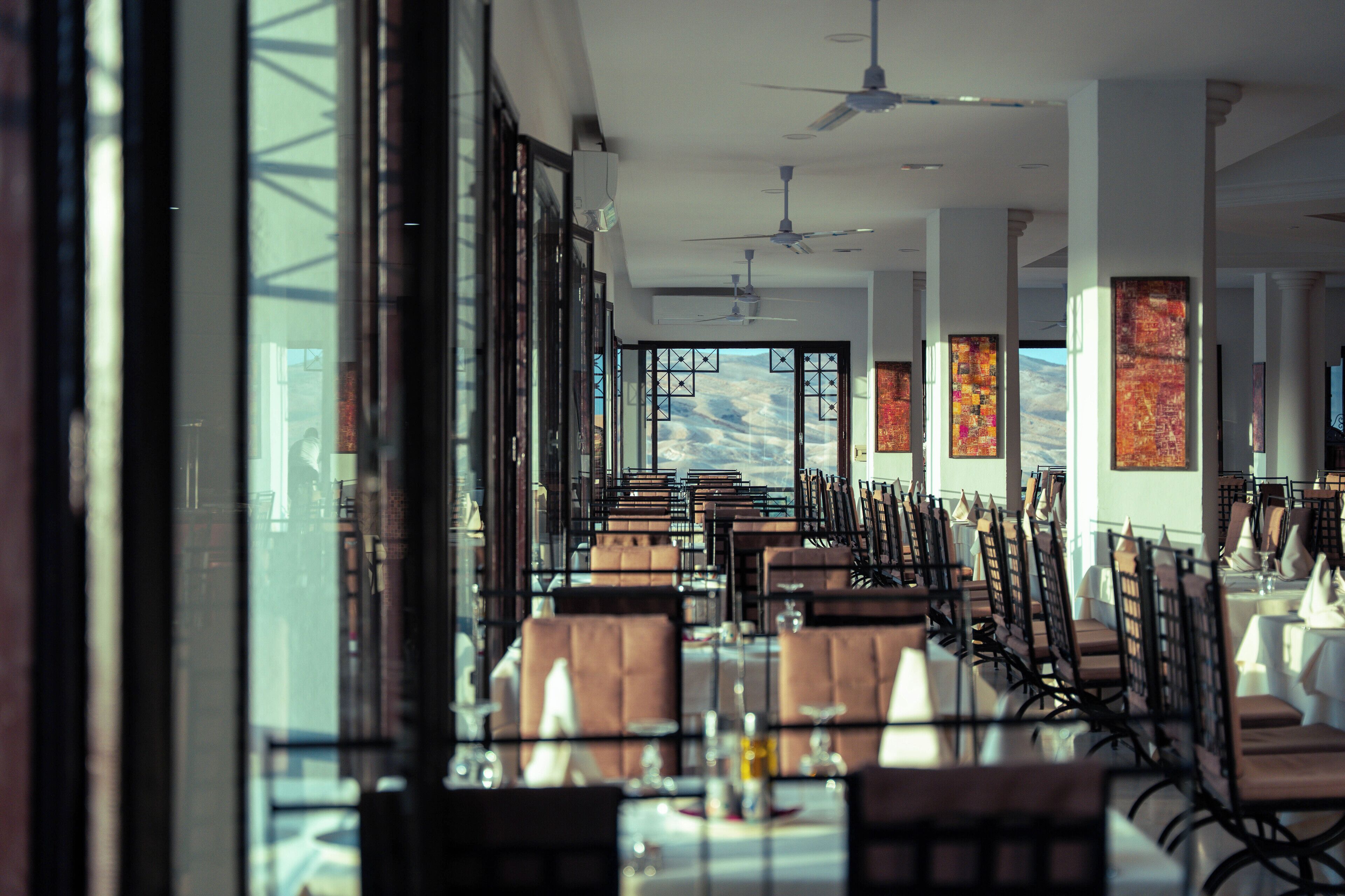 A restaurant with long tables and chairs, large windows, and ceiling fans.