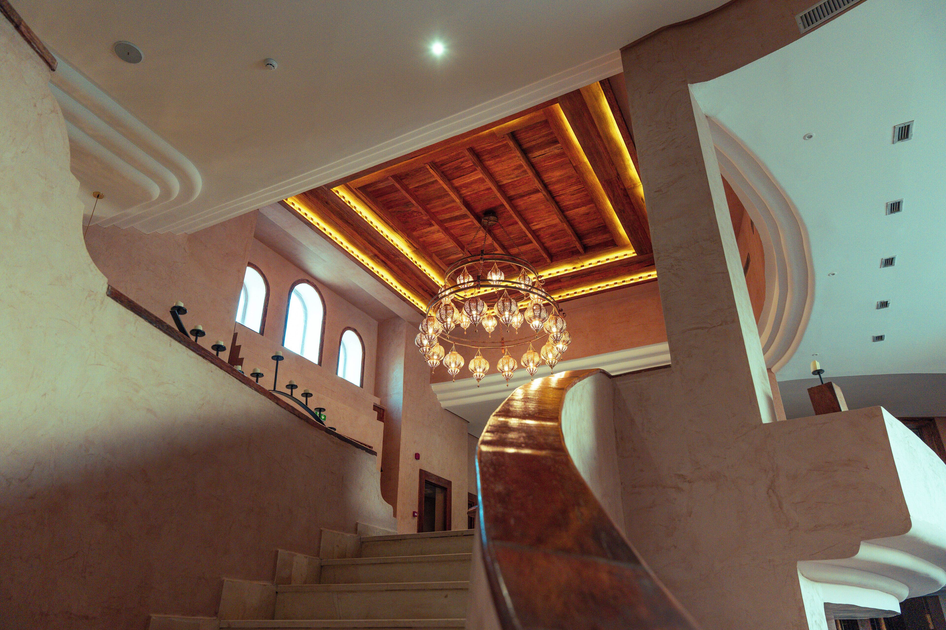 A grand staircase with a wooden finish and a large chandelier.