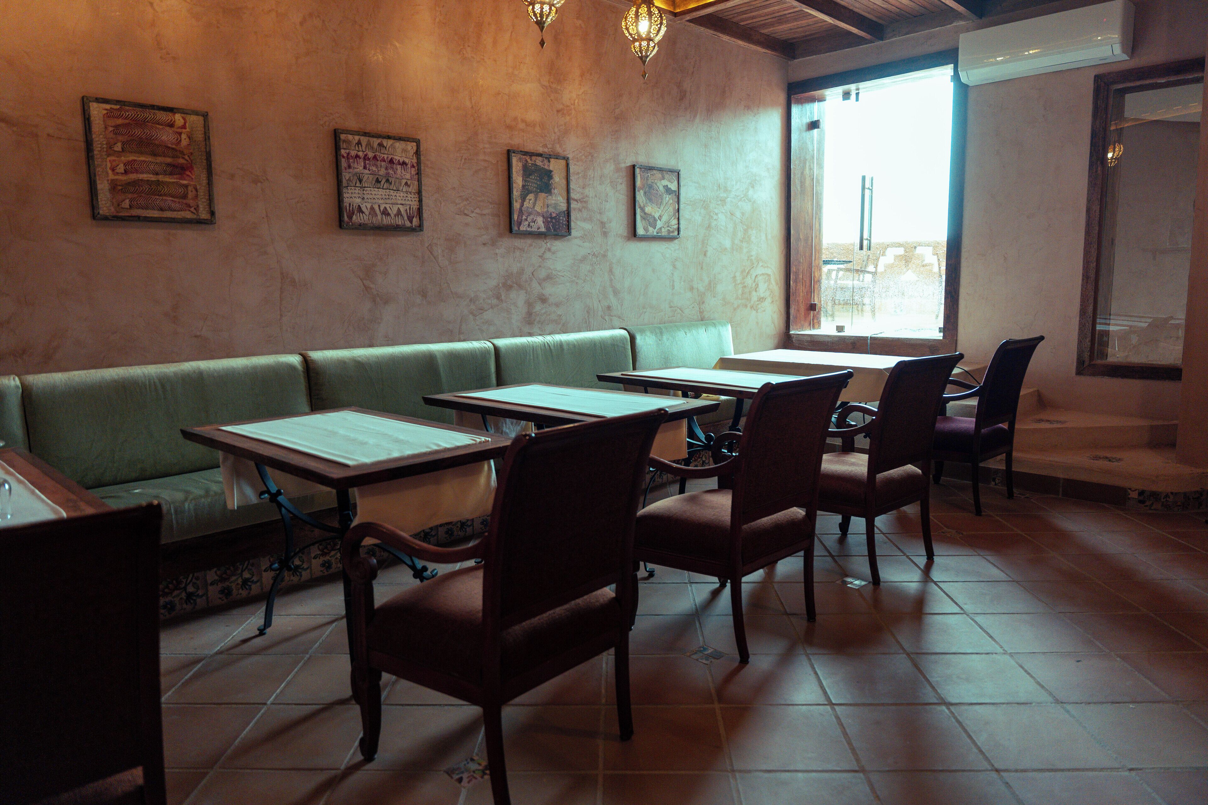 A restaurant interior with a green booth seating area, wooden tables, and chairs.