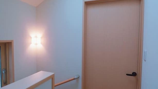 Un couloir avec une porte en bois, un luminaire fixé au mur et une main courante.