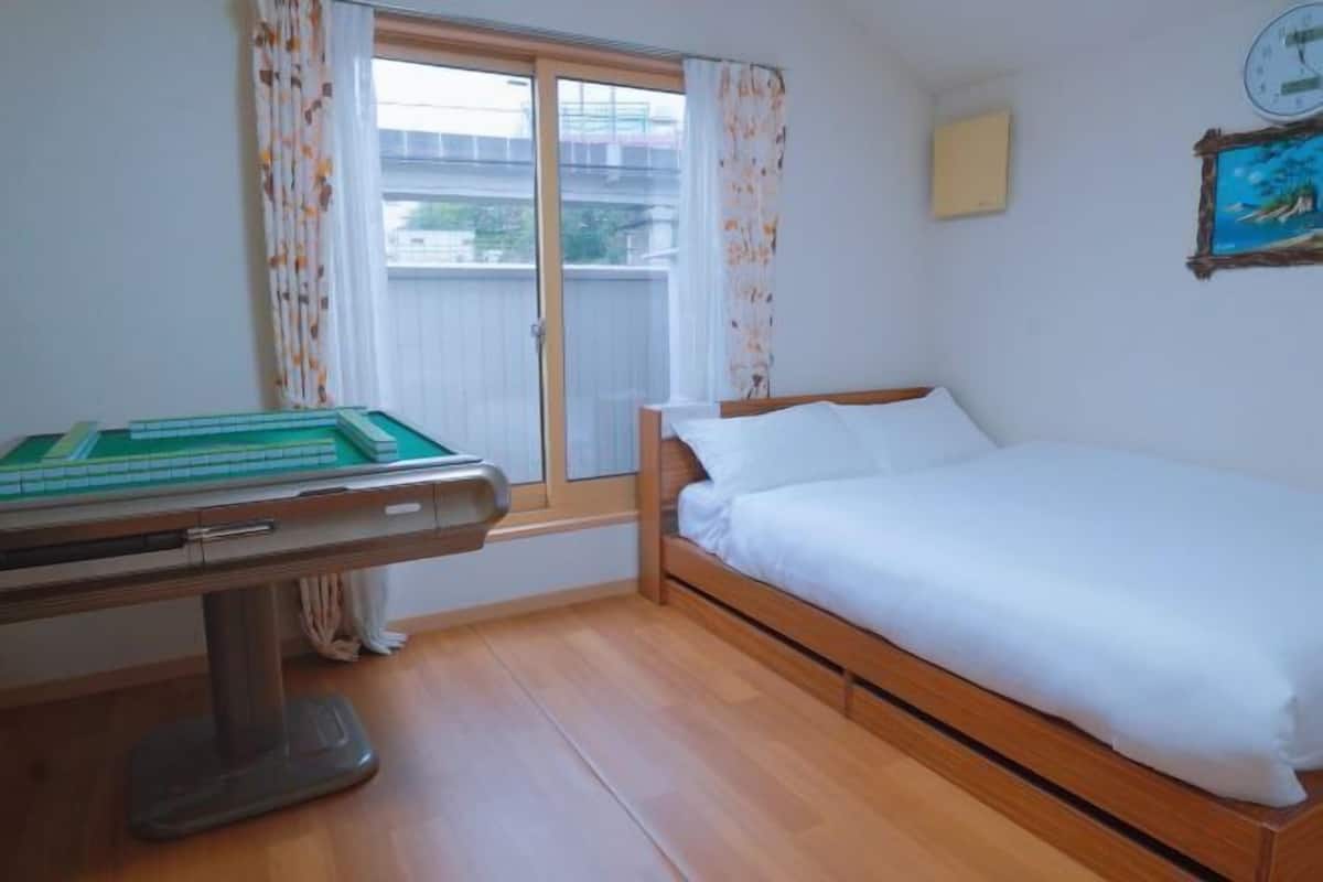 Una habitación con una cama, una mesa de billar, un ventanal con cortinas y un reloj en la pared.