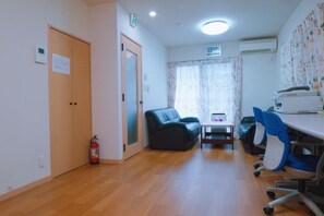 A room with a wooden floor, a black sofa, a desk with a computer, and a fire extinguisher.