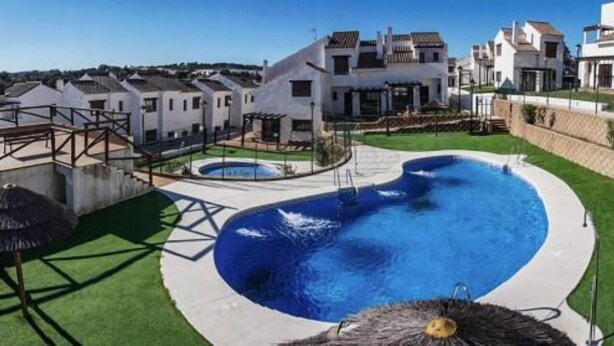 Una piscina amb disseny de cor, envoltada per un jardí ben cuidat i un edifici blanc amb diverses finestres.