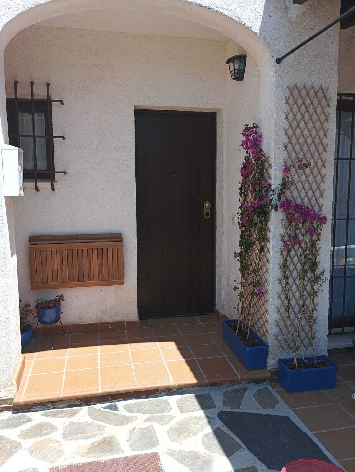 Une entrée d’immeuble avec une porte sombre, un banc en bois et des plantes en pot.