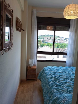 A bedroom with a bed, a window with a view, a lamp, and a mirror.