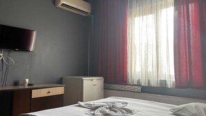 A hotel room with a bed, a desk, a television, an air conditioner, and a window with curtains. - Prenses otel (Ankara)