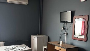 A hotel room with two beds, a desk, a chair, a heater, a television, and a clock on the wall. - Prenses otel (Ankara)