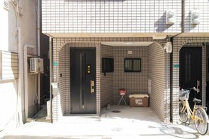 A building entrance with a tiled facade, a black door, and a bicycle parked outside. - Younoyado (Osaka)