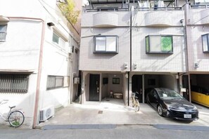 A residential building with a garage, a bicycle, and a parked car. - Younoyado (Osaka)