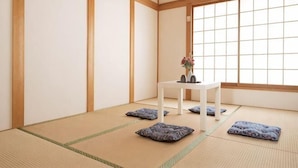 A tatami mat room with a low table, cushions, and a window. - Younoyado (Osaka)