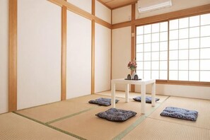 A tatami mat room with a low table, cushions, and a window. - Younoyado (Osaka)