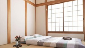 A traditional Japanese room with tatami flooring, a low bed, a window with shoji screens, and a small vase with flowers. - Younoyado (Osaka)