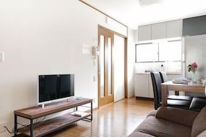 A modern living room with a flat-screen TV on a wooden stand, a sofa, and a dining area with a table and chairs. - Younoyado (Osaka)