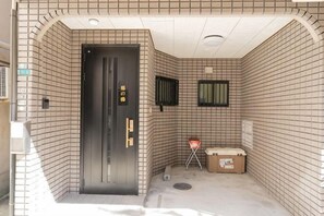 A hotel entrance with a black door, tiled walls, a small window, and a trash bin. - Younoyado (Osaka)